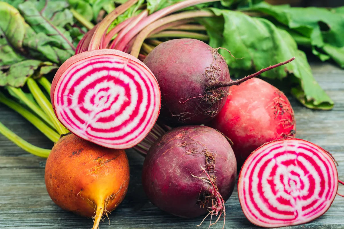 Fresh sunchokes, also known as Jerusalem artichokes, with some cut in half showing white and pink rings, on a wooden surface.